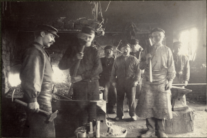 Eine Gruppe von Männern in einer Schmiede, jeder hält einen Hammer in der Hand.