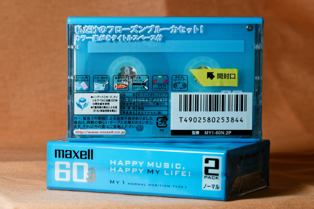 Blue Maxell "Happy Music Happy My Life" Kassettenband auf einem braunen Tisch mit einem leicht unscharfen, verträumten Hintergrund.