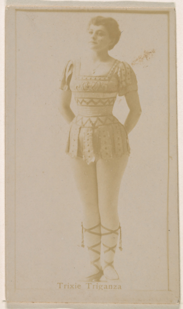 Ein altes Foto einer Frau in einem hellfarbenen gemusterten Badeanzug, ihre Haare zu einem Dutt gebunden, die direkt in die Kamera schaut.