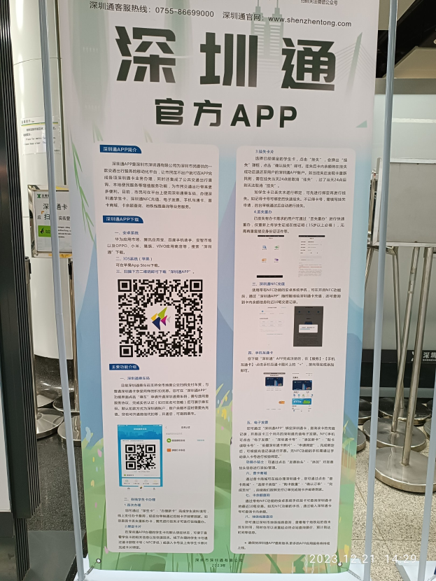 Banner mit einem QR-Code vor einem Gebäude, wahrscheinlich für den Shenzhen International Airport beworben, umgeben von Ständen und Schildern.