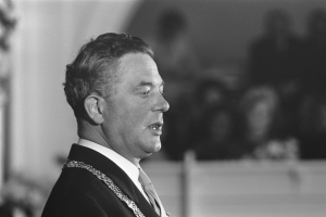 Ein Mann in Anzug und Krawatte steht an einem Podium mit einem Mikrofon und spricht zu einer unscharfen Menge, der ein Politiker zu sein scheint.