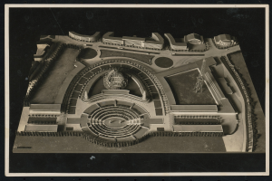 Schwarzes und weißes Rahmenfoto eines detaillierten Modellkonzertsaals mit einer zentralen Kuppel, steinernen Wänden, Metalldach und einer hell erleuchteten Bühne, umgeben von einer Menge.