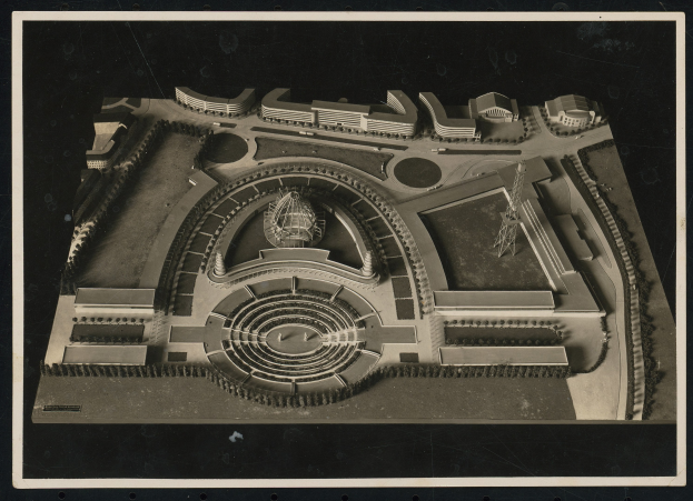 Schwarzes und weißes Rahmenfoto eines detaillierten Modellkonzertsaals mit einer zentralen Kuppel, steinernen Wänden, Metalldach und einer hell erleuchteten Bühne, umgeben von einer Menge.