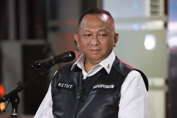 Ein Mann in schwarzer Weste und weißem Hemd steht vor einem Mikrofon und sieht besorgt aus, mit einem unscharfen Hintergrund.