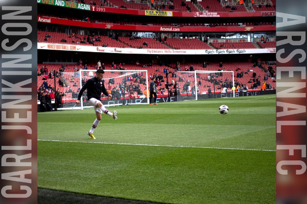 Ein Fußballspieler, der einen Ball in einem Stadion mit Torpfosten und Zuschauern im Hintergrund tritt.