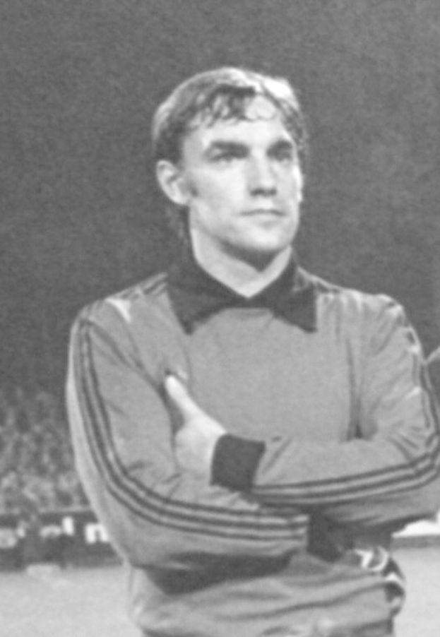 Schwarzes und weißes Foto eines Mannes auf einem Fußballfeld mit verschränkten Armen, umgeben von sitzenden Zuschauern, der legendäre Manchester United-Torhüter, der im Alter von 89 Jahren verstorben ist.