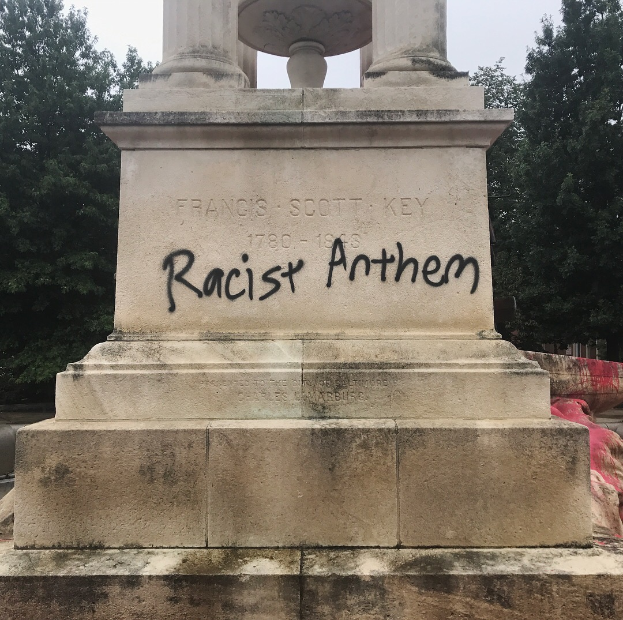 Ein Denkmal mit der Inschrift 'Rassistischer Anthem' umgeben von Bäumen unter einem klaren Himmel.