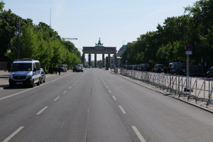 Ein Polizeiwagen steht auf der Seite einer vielbefahrenen Straße vor dem Brandenburger Tor in Berlin, Deutschland, mit Barrieren, Schildern, Bäumen und Laternenmasten im Hintergrund und einer bewölkten Himmel.