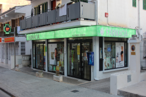 Apotheke an einer Straßenecke mit Gebäuden, Fahrzeugen und einem klaren Himmel.