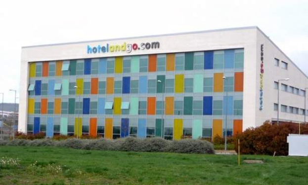 Großes modernes Hotelgebäude mit vielen Fenstern, umgeben von Grünflächen, Fahrzeugen und einem bewölkten Himmel; Text an dem Gebäude lautet "hotel und go".