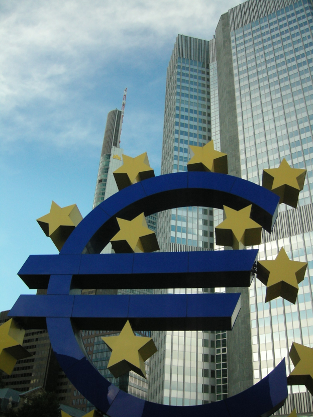 Eurozeichen vor dem Hauptgebäude der Europäischen Zentralbank in Frankfurt, Deutschland, mit Bäumen und einem bewölkten Himmel.