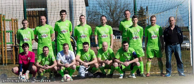 Eine Gruppe von Männer in grünen T-Shirts steht auf einem Fussballfeld, einige hocken, mit einem Ball vor ihnen und einem Torpfosten rechts daneben.